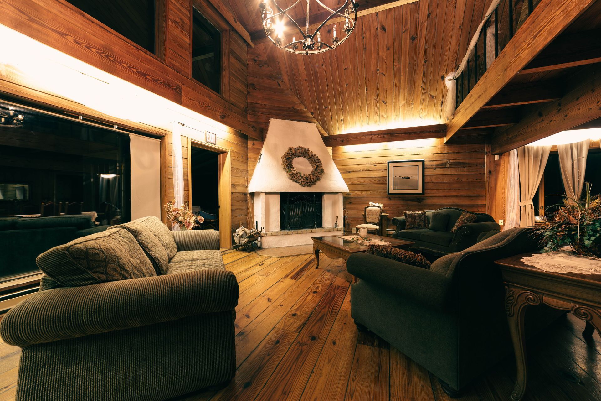 Warm rustic cabin living room with wood-paneled walls, stone fireplace, and cozy sofas under a chandelier