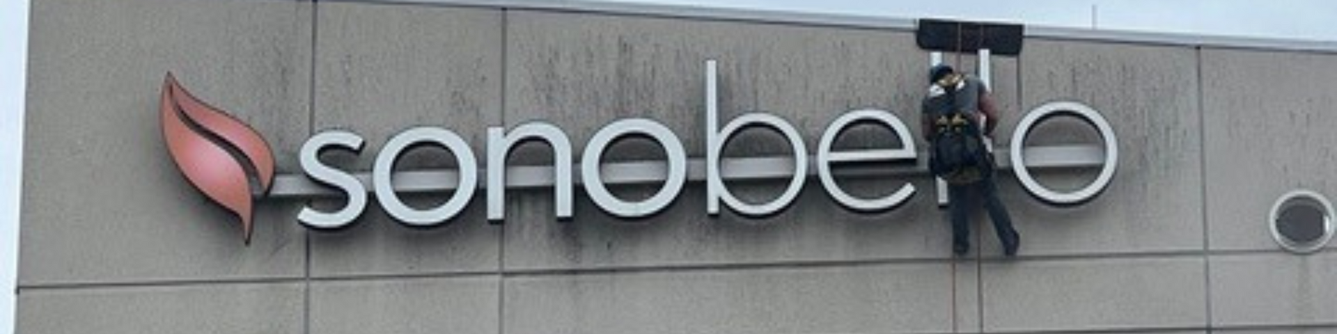 A man is cleaning the sign on the side of a building.