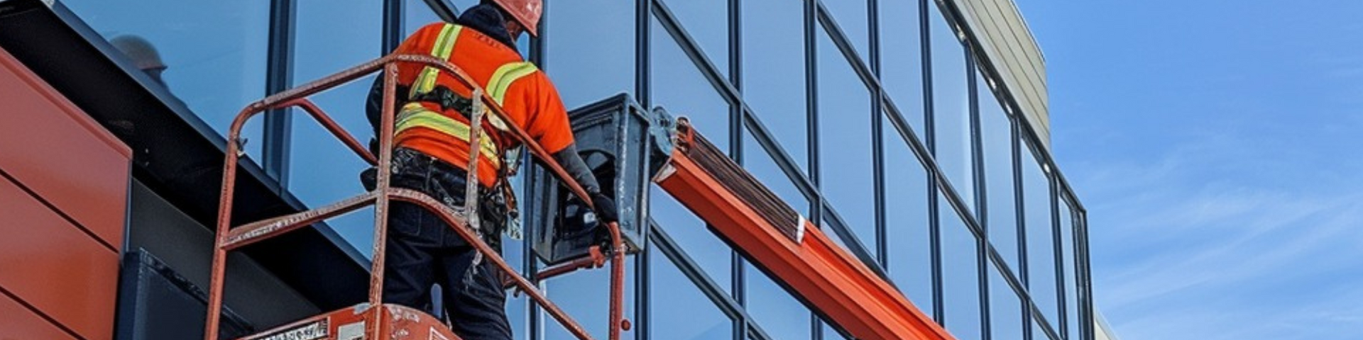 A man is standing on a crane cleaning the windows of a building.