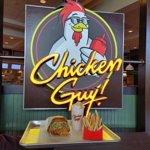 A chicken guy sign hangs above a tray of food