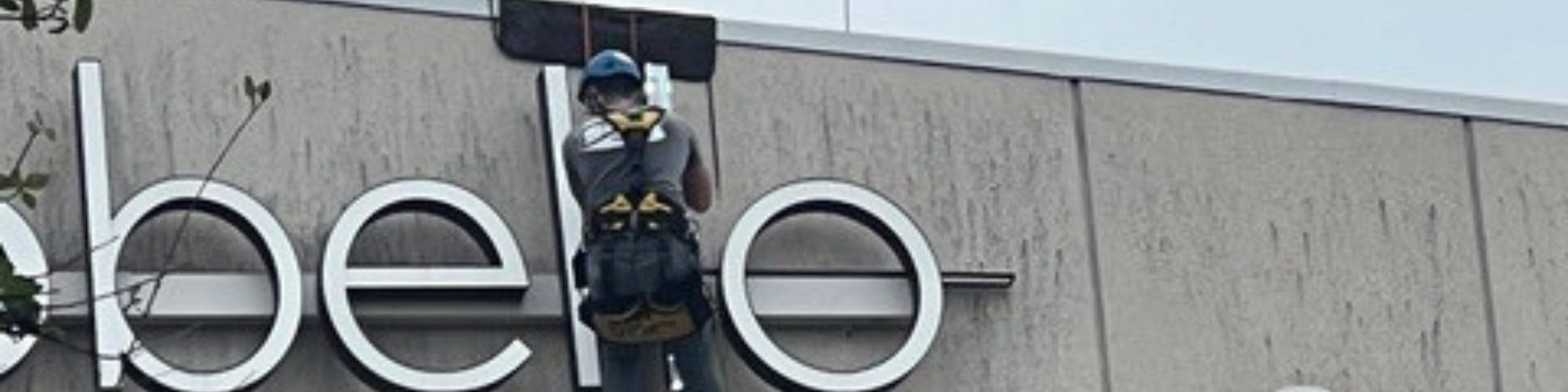 A man is climbing up the side of a building to install a sign.