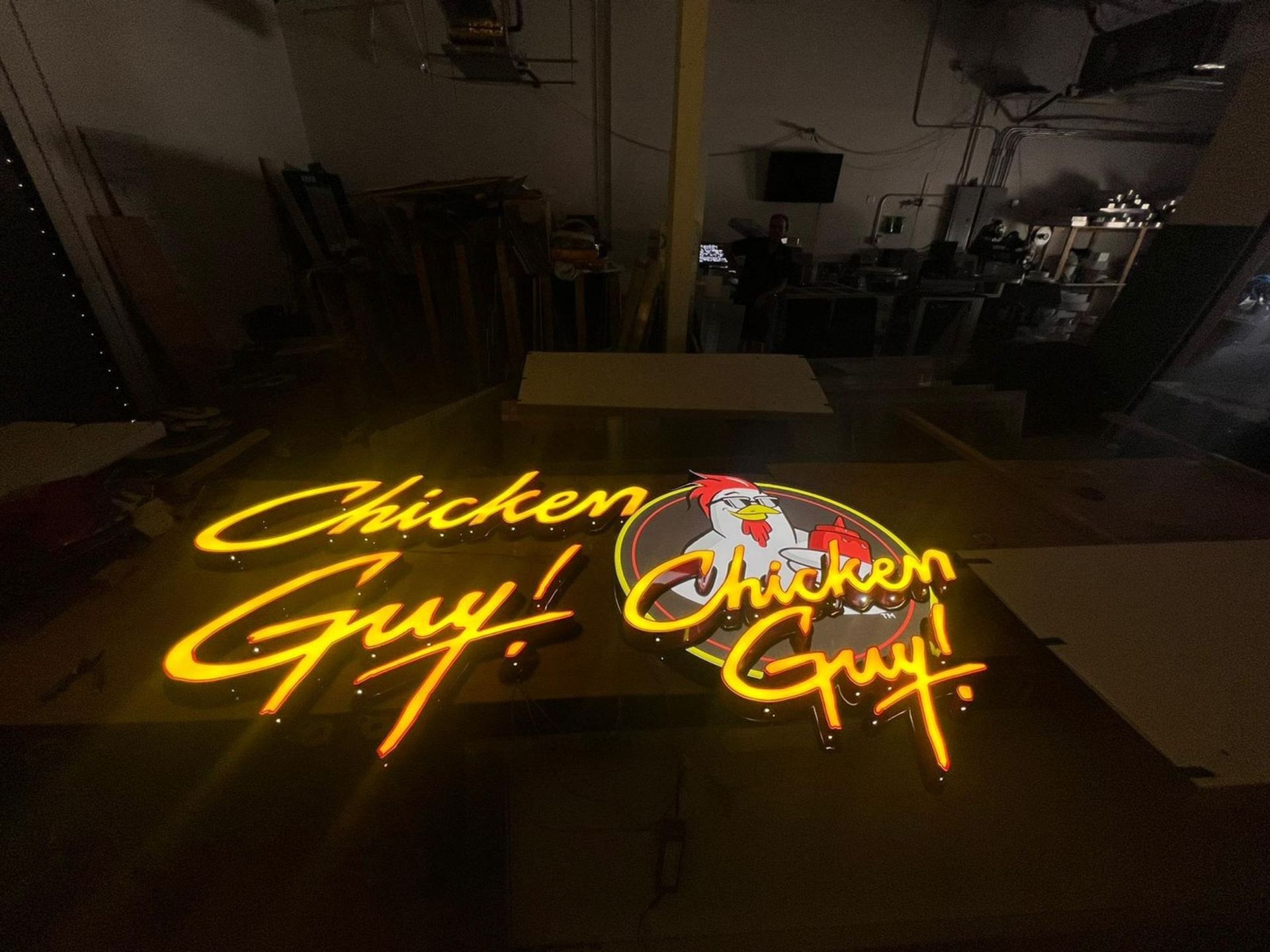A neon sign for chicken guy is lit up in a dark room