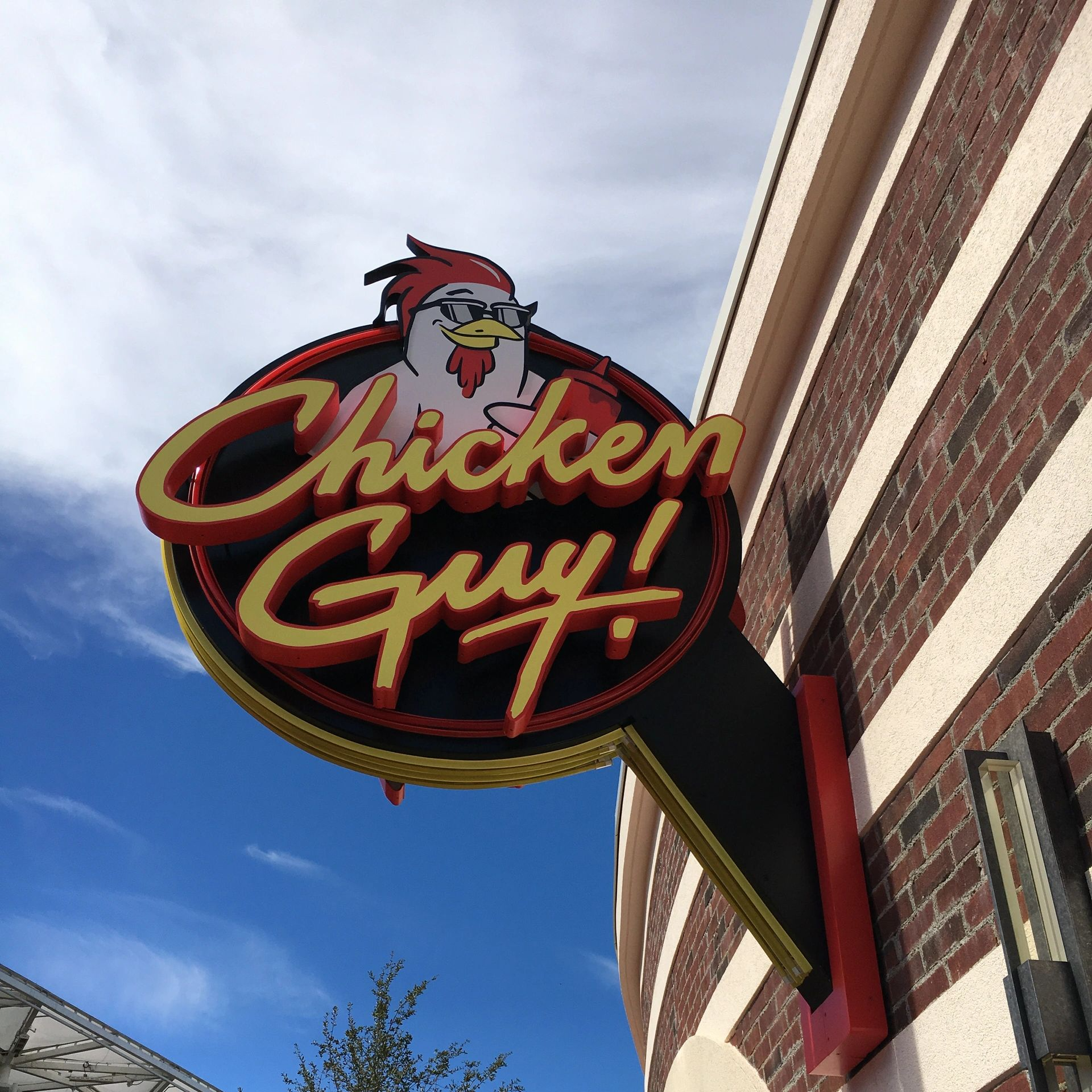 A chicken guy sign hangs from the side of a brick building