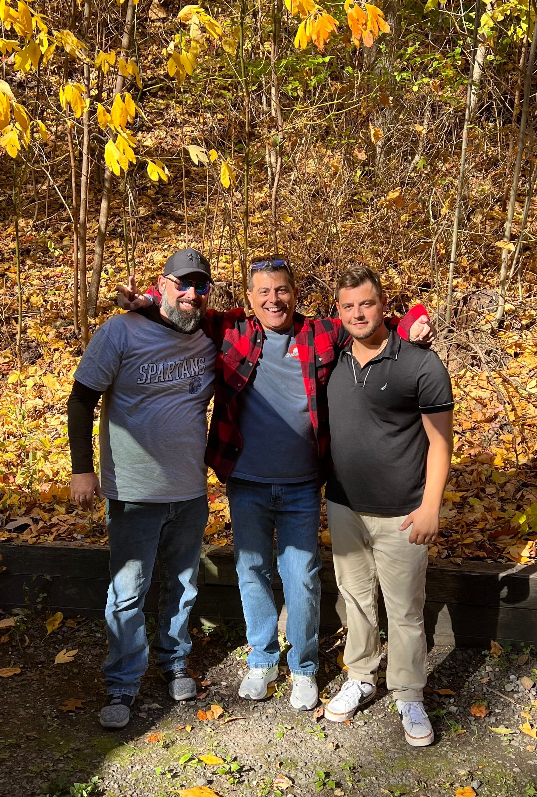 Three men are posing for a picture in the woods.