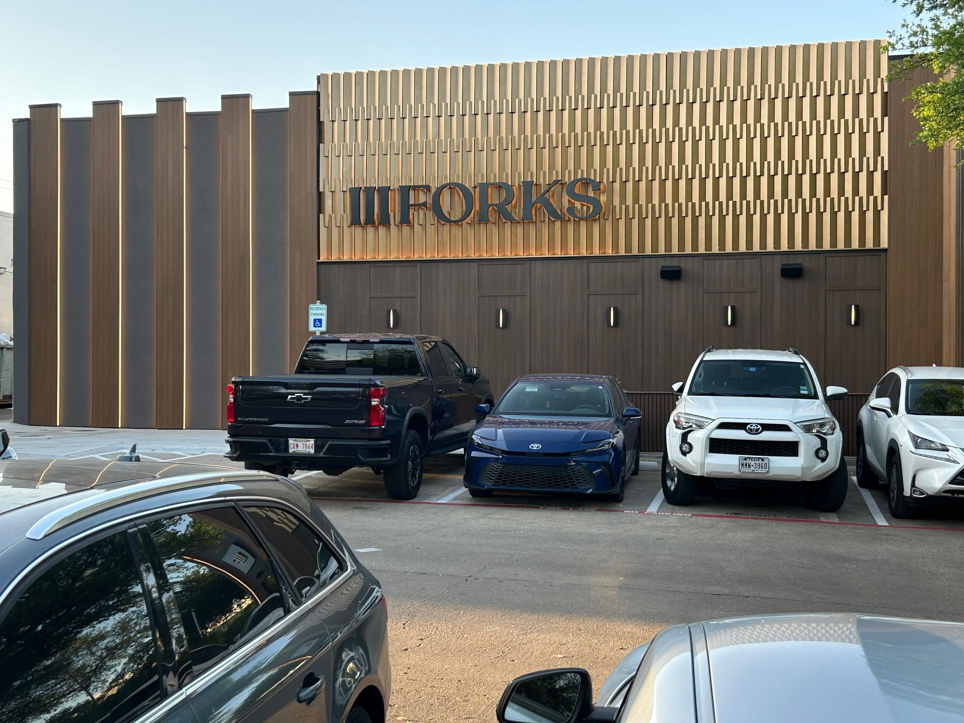 A row of cars are parked in front of a building that says forks.