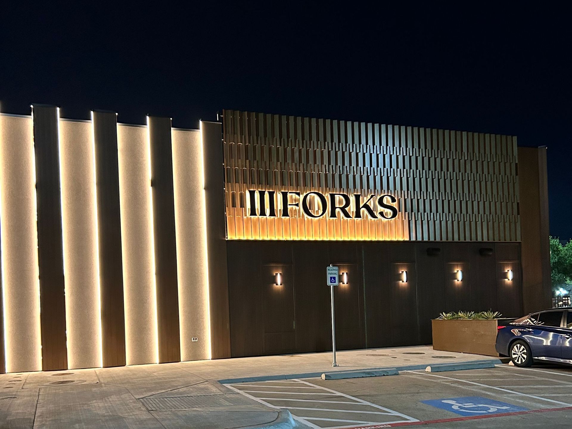 A car is parked in front of a building that says iii forks