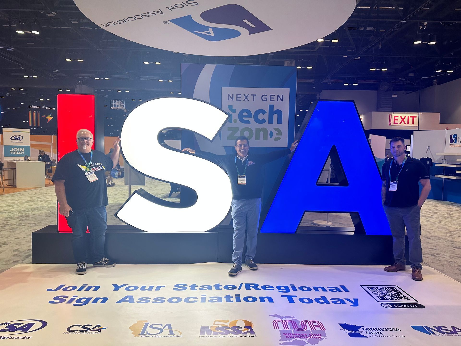 Three men are standing in front of a sign that says isa