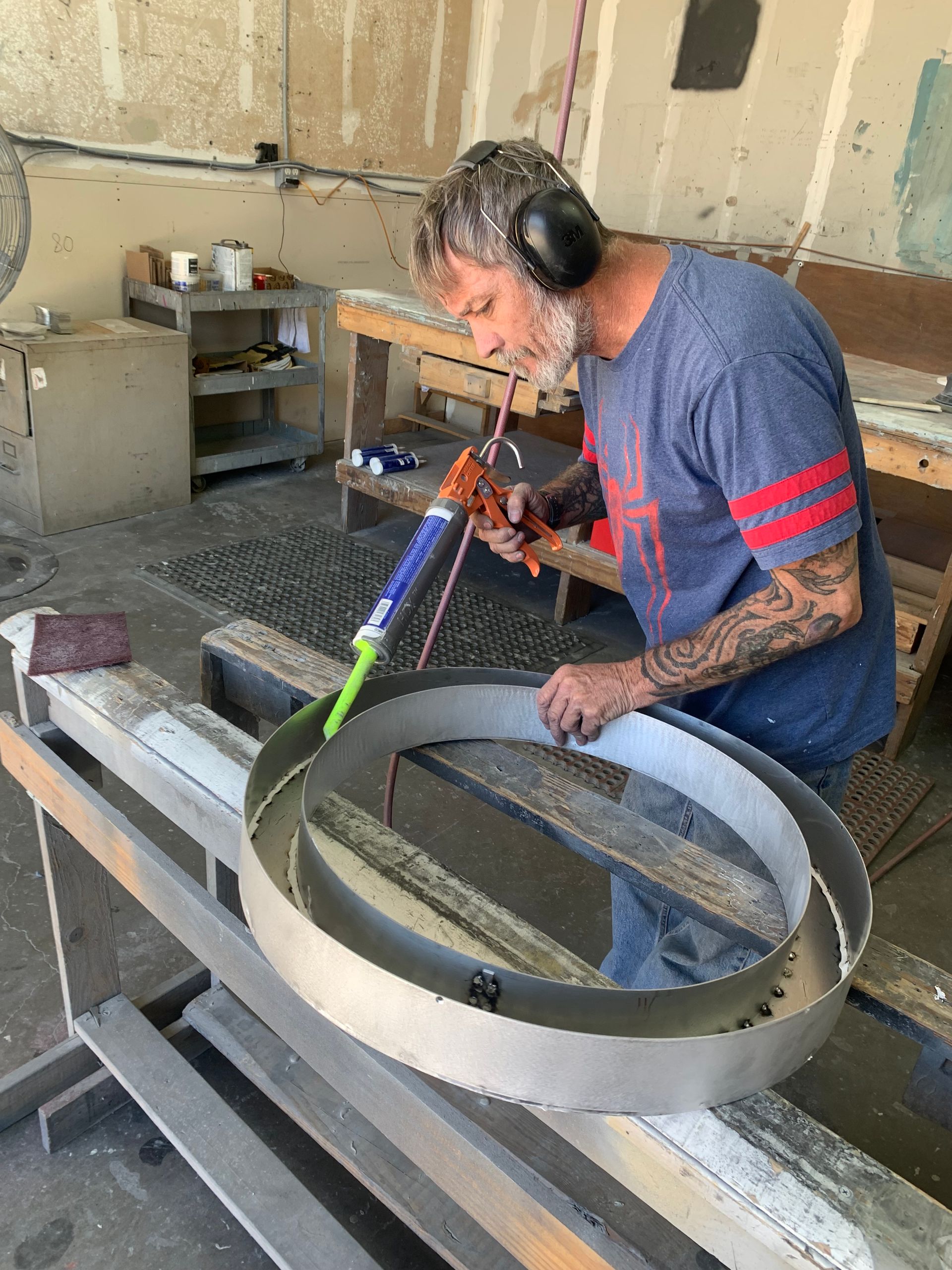 A man wearing headphones is working on a metal ring in a workshop.