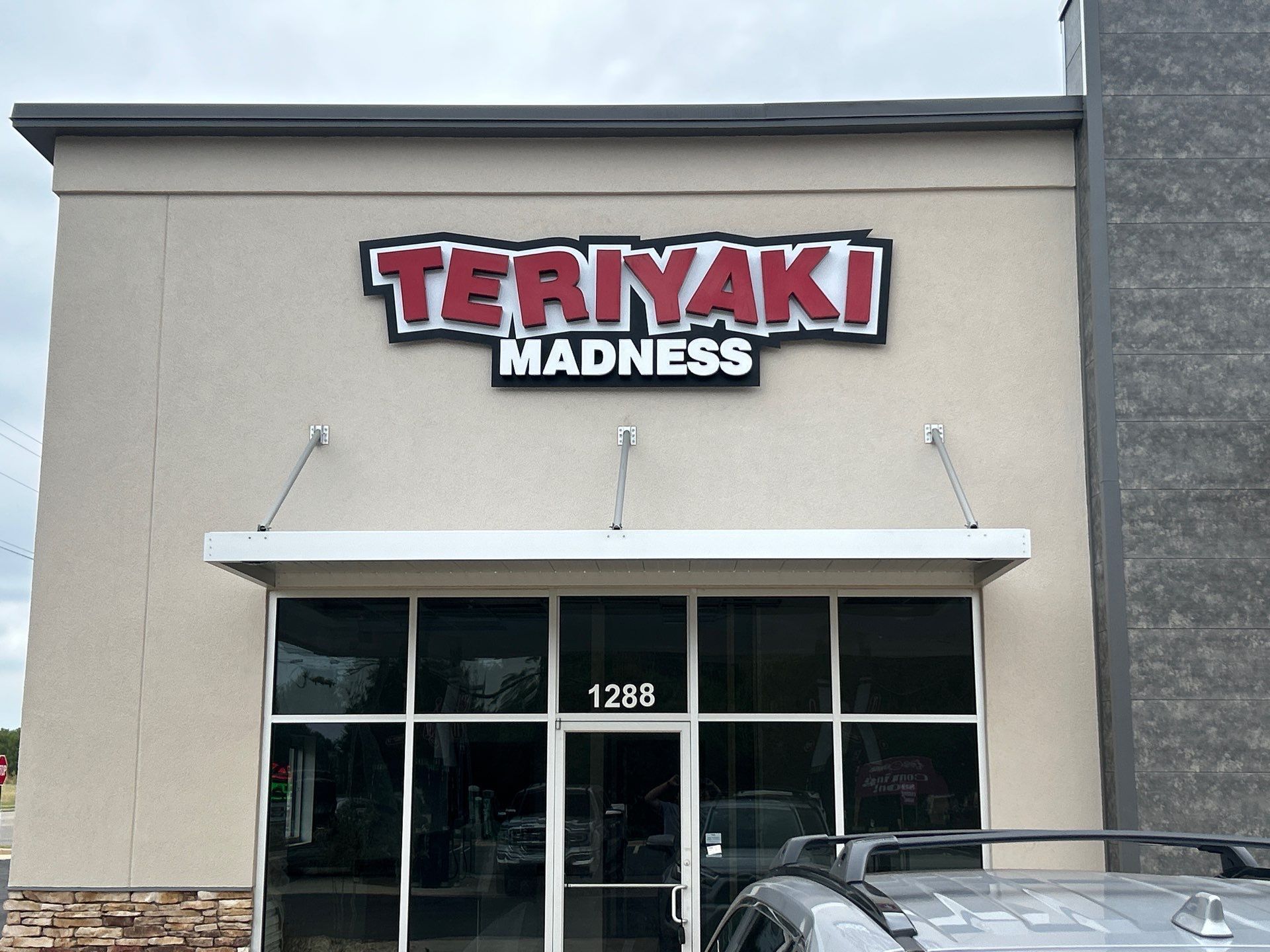 Teriyaki Madness restaurant sign above glass front doors. Cream building with awning.