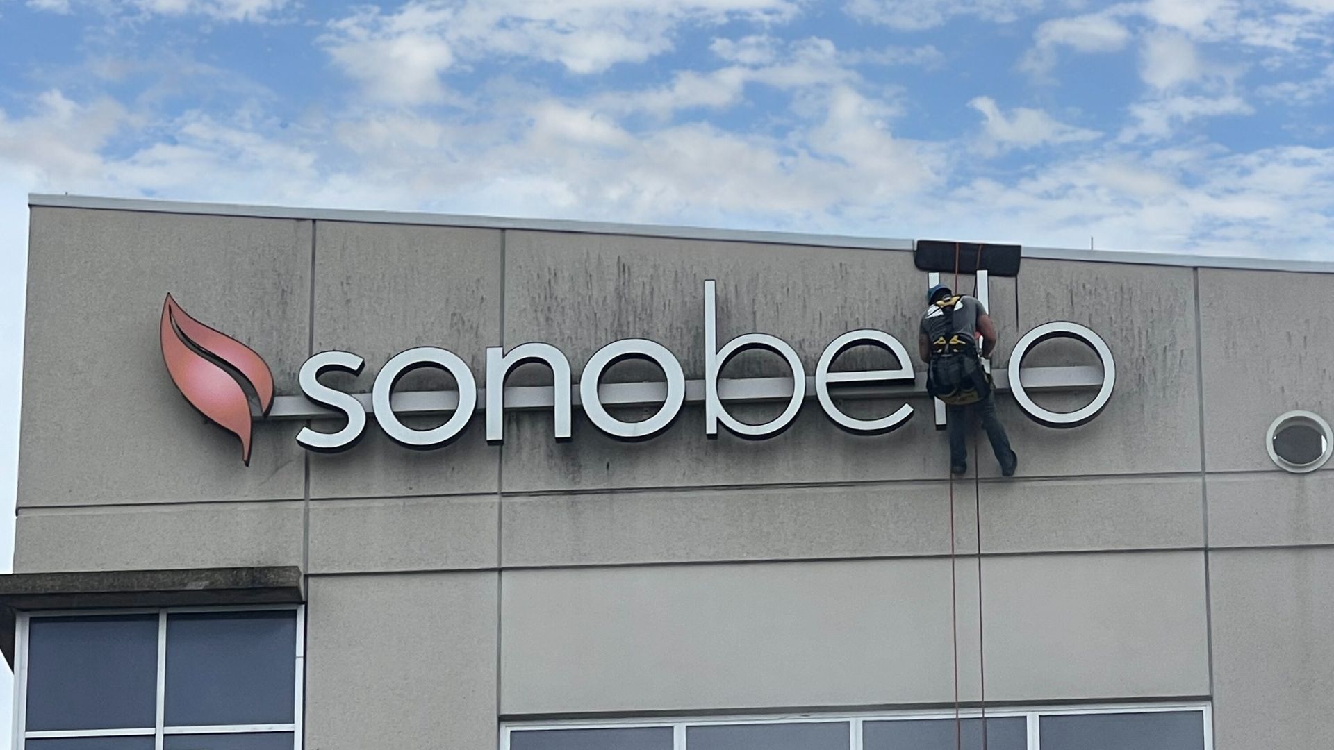 A man is cleaning the sign on the side of a building.