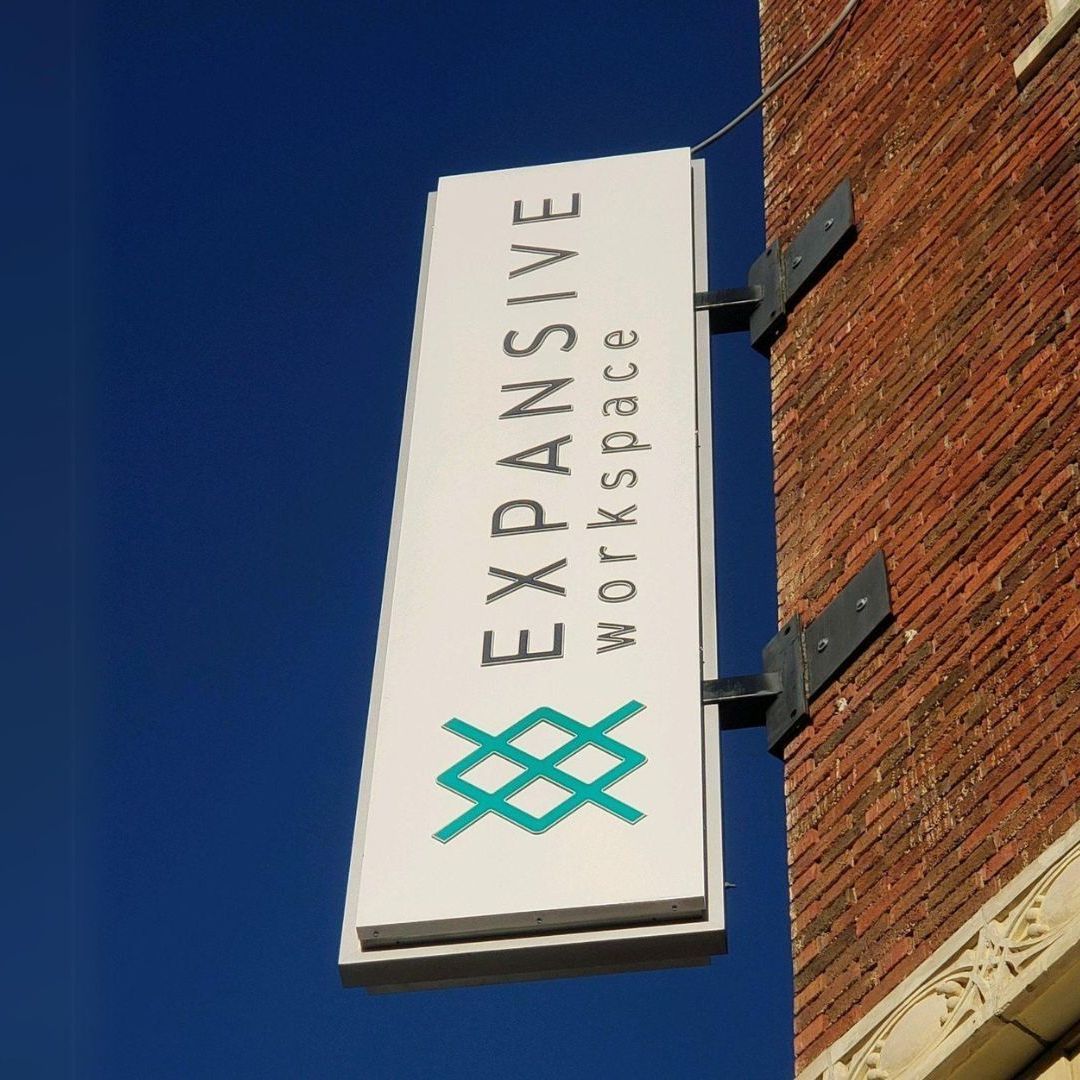 An expandive workspace sign hangs from a brick building
