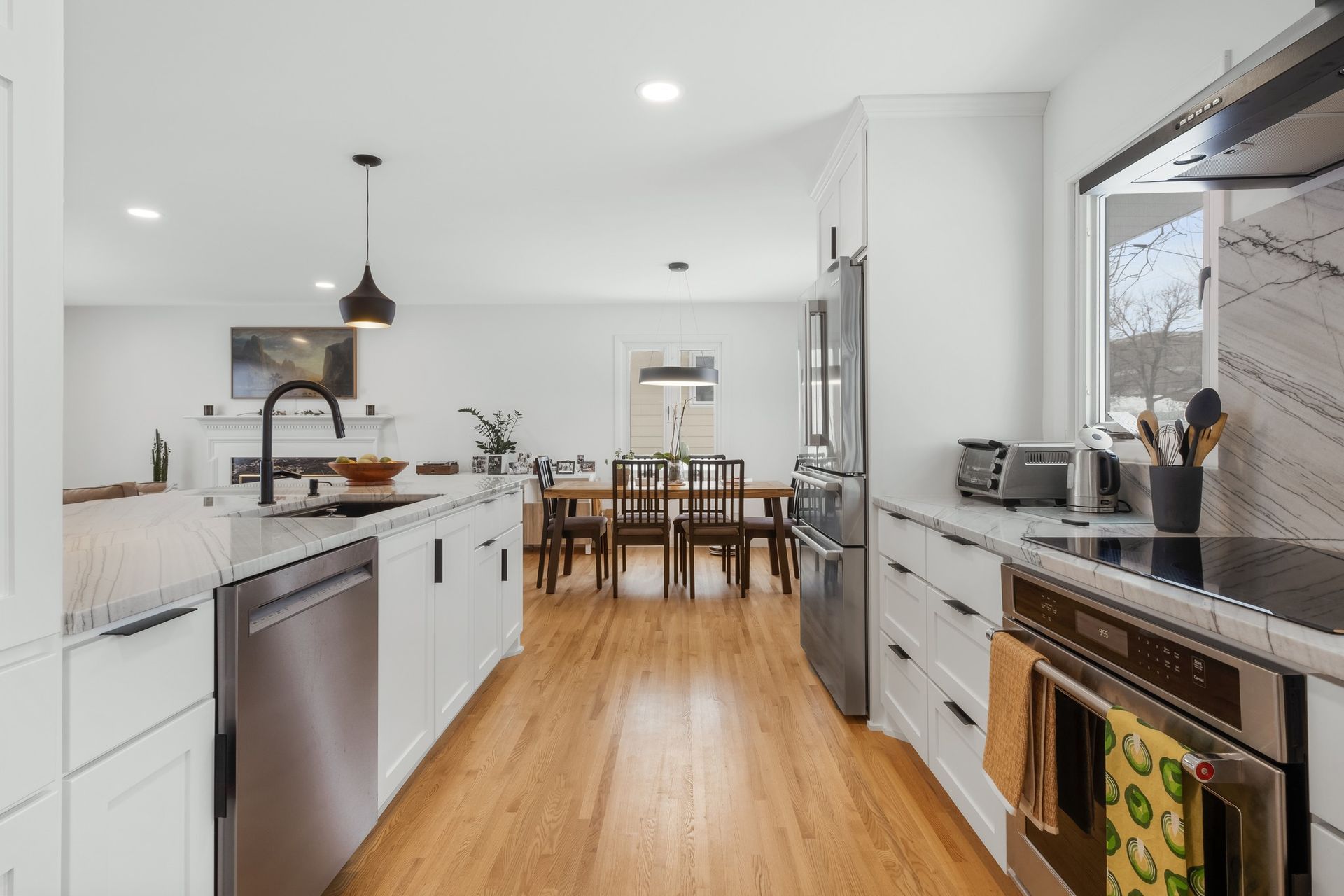 Modern kitchen with white cabinets, stainless steel appliances, and wood flooring leading to dining area.