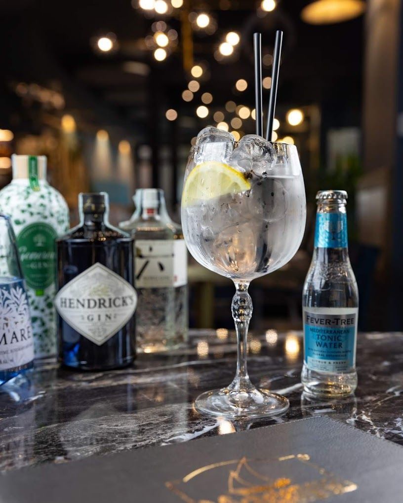 Un bicchiere di gin tonic con ghiaccio e una cannuccia su un tavolo.