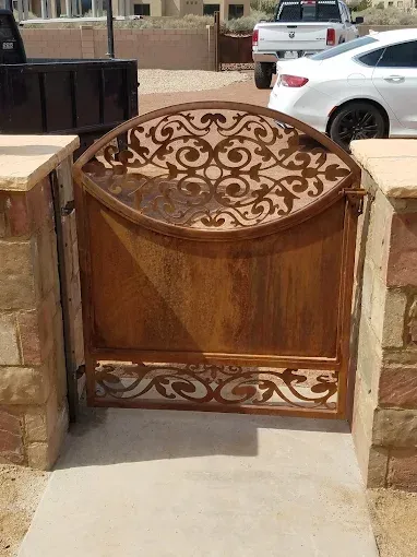 Rust-colored ornate metal gate between stone pillars at a driveway entrance