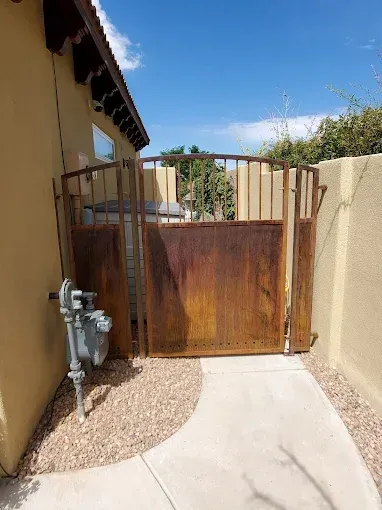 Narrow concrete walkway leading to a wooden gate between tan stucco walls, with a utility meter on the left.