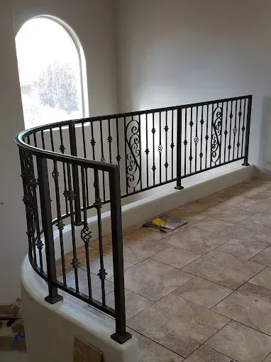 Stair landing with black wrought-iron railing beside an arched window and tiled floor