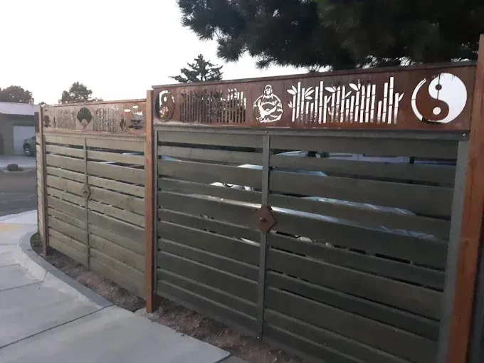 Wooden driveway gate with decorative panels and white symbols beside a sidewalk