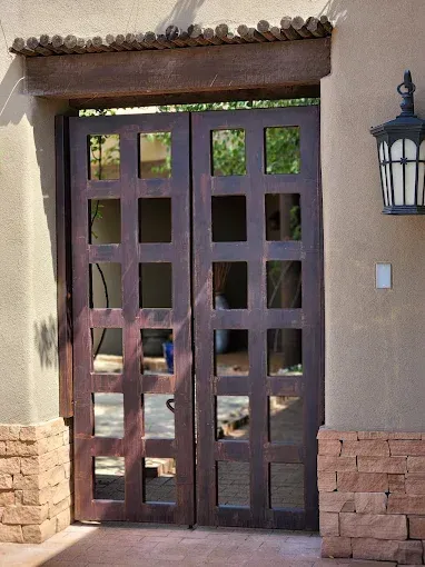 Dark wooden double doors with small windows set in a stucco wall, with a lantern on the right.