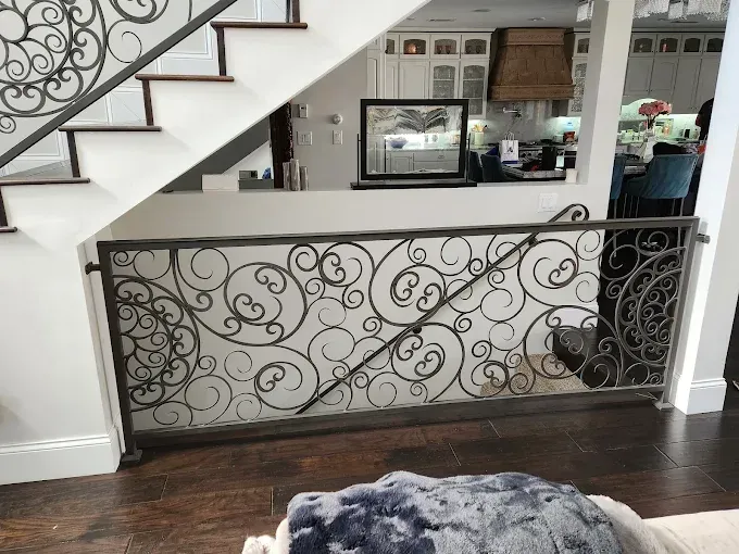 Interior staircase with ornate black railing overlooking a kitchen and dark wood floor beneath a fur rug