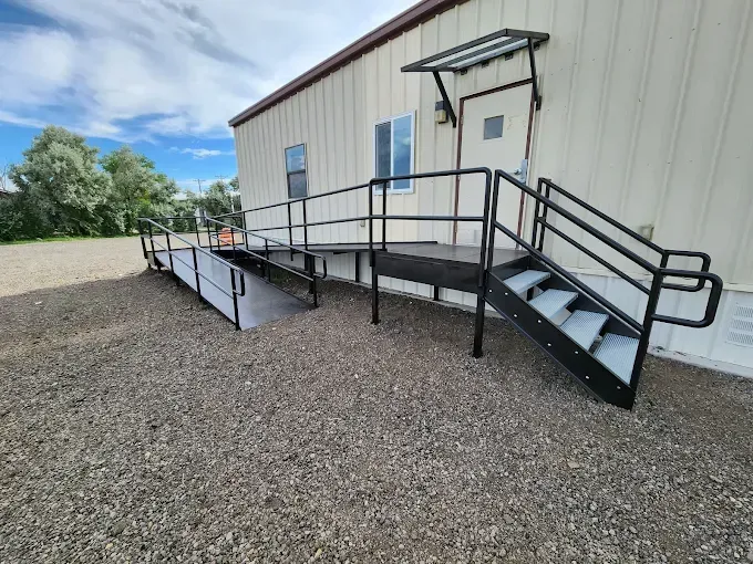 Accessible ramp and stairs with black railings leading to a beige building on gravel.