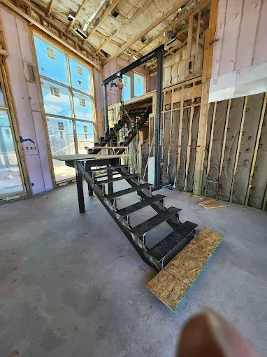 Exposed construction interior with a black metal staircase and open framing near large windows