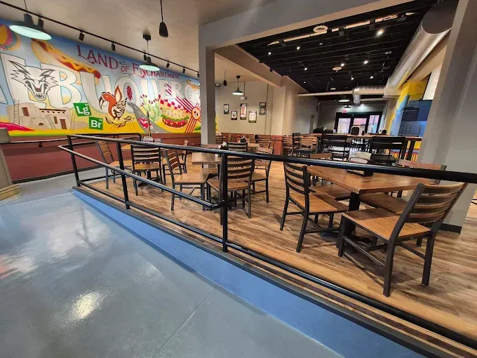 A raised dining area in a restaurant with tables, wooden chairs, and a large, colorful mural on the back wall.