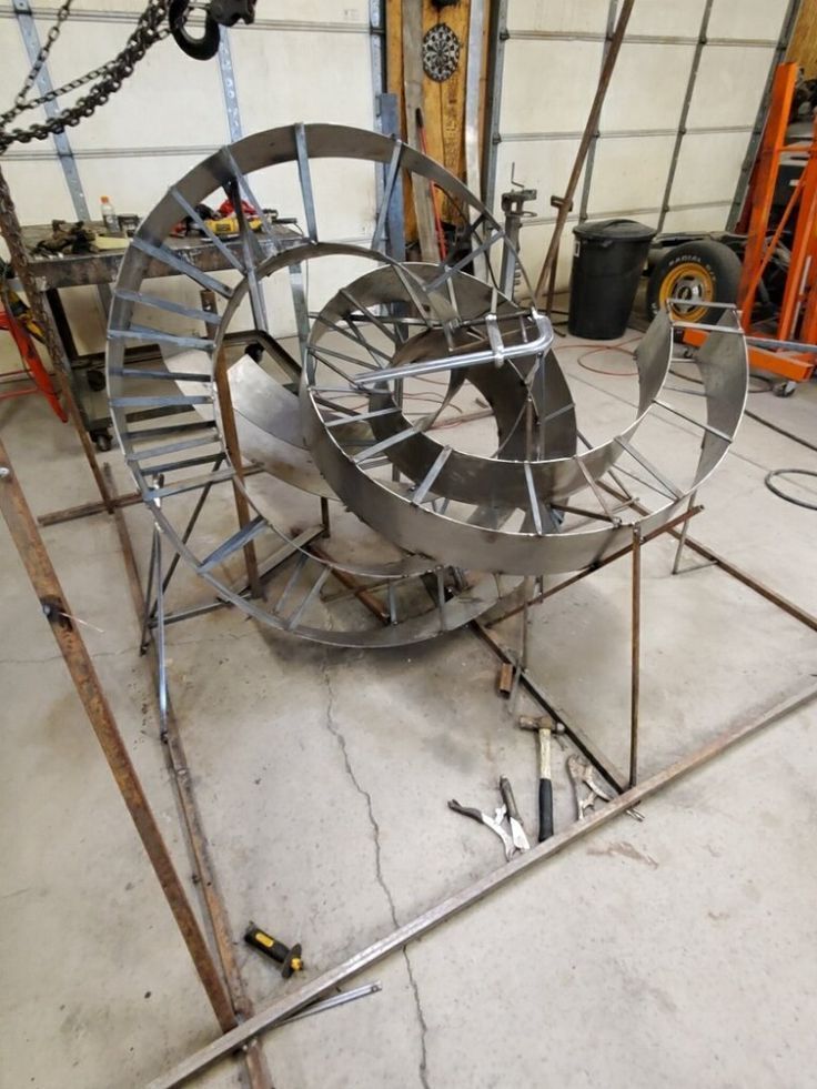 Large metal spiral sculpture with concentric rings on a stand in a workshop or studio.