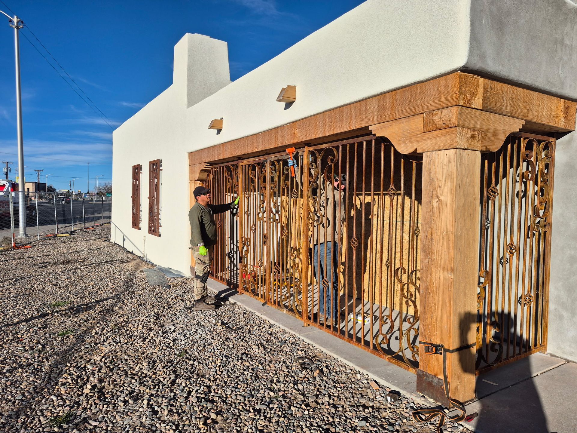 Person beside a boarded-up window on a white building in a gravel lot under a clear blue sky