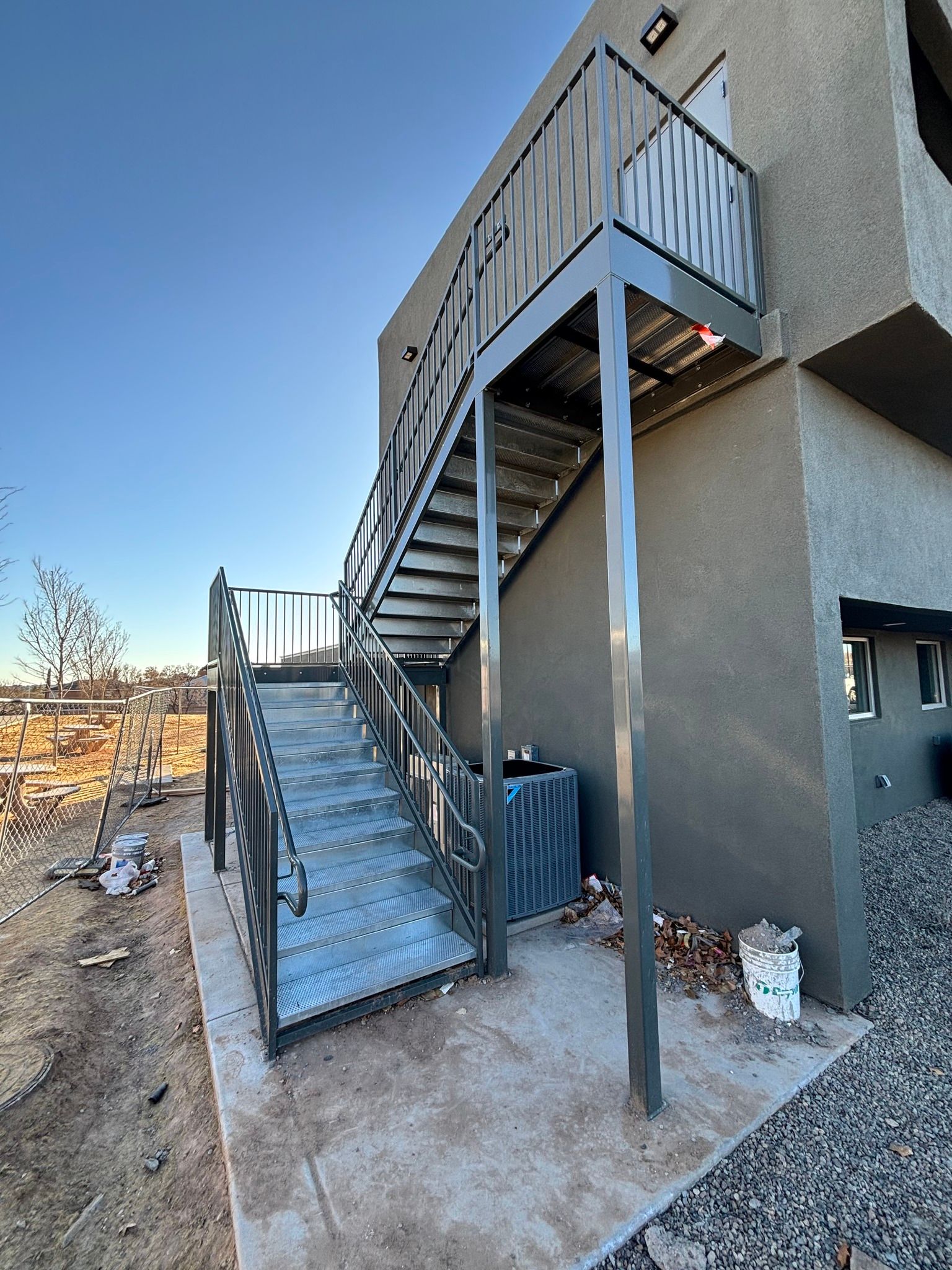 Outdoor metal staircase and elevated walkway beside a gray building under construction.