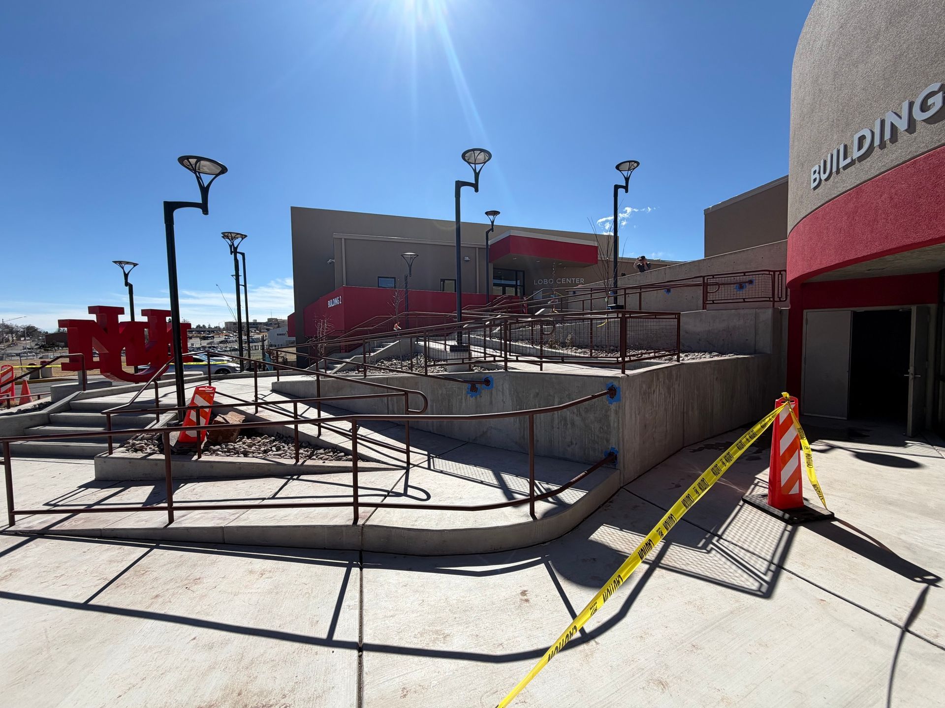 Sunny outdoor retail area with ramp railings, red awnings, and a building entrance blocked by caution tape.