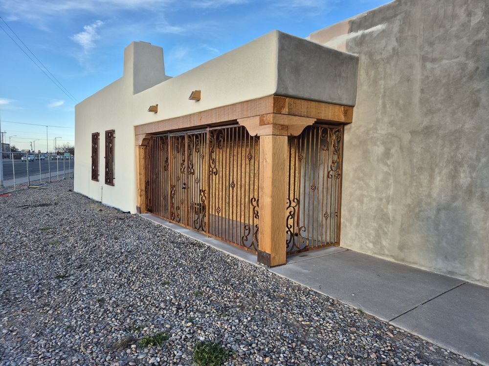 Small white building with wooden lattice porch beside a concrete wall on a gravel lot