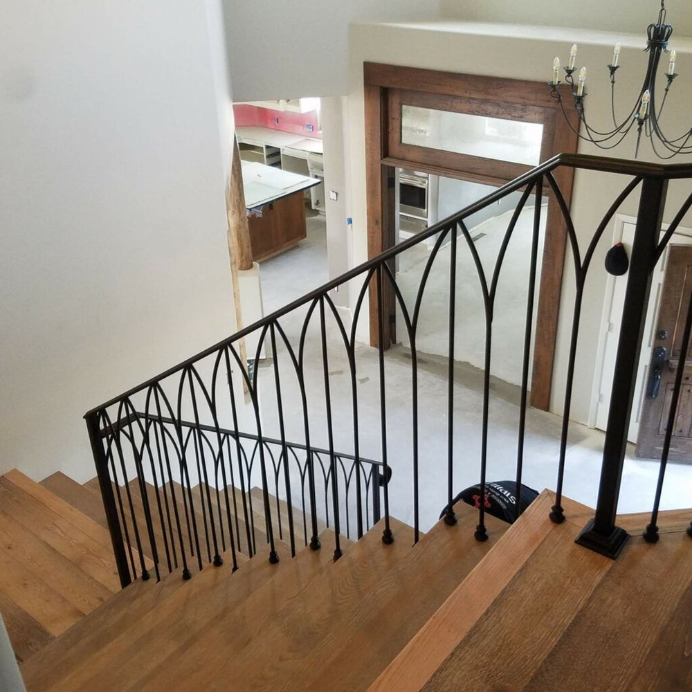 Staircase with wooden steps and black wrought-iron railing, looking down into a bright entryway.