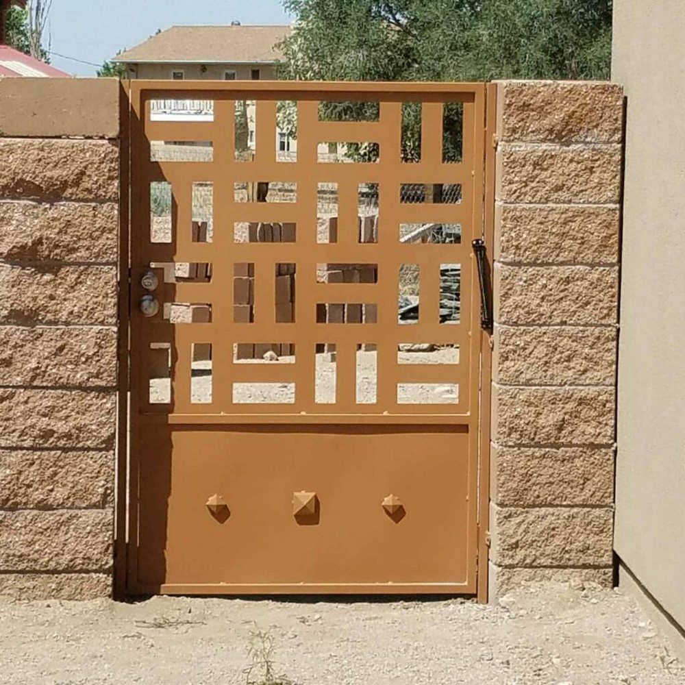 Brown metal gate set in a stone wall, with geometric cutouts and sunlight casting shadows.