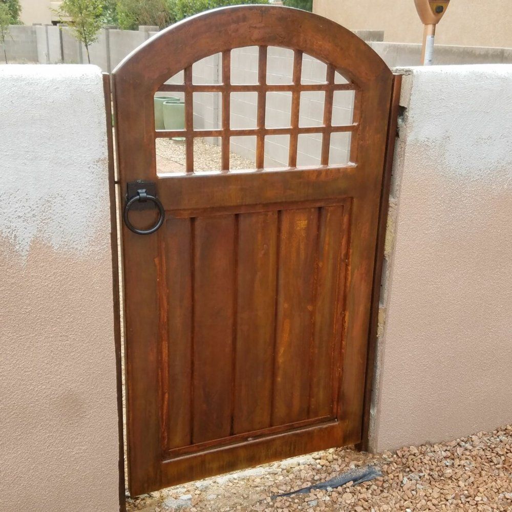 Wooden arched garden gate set in a white stucco wall with a black ring handle