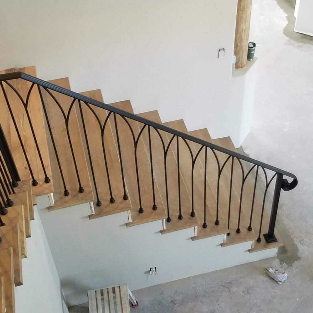 Curved staircase with black wrought-iron railing and light wood steps in a bright interior