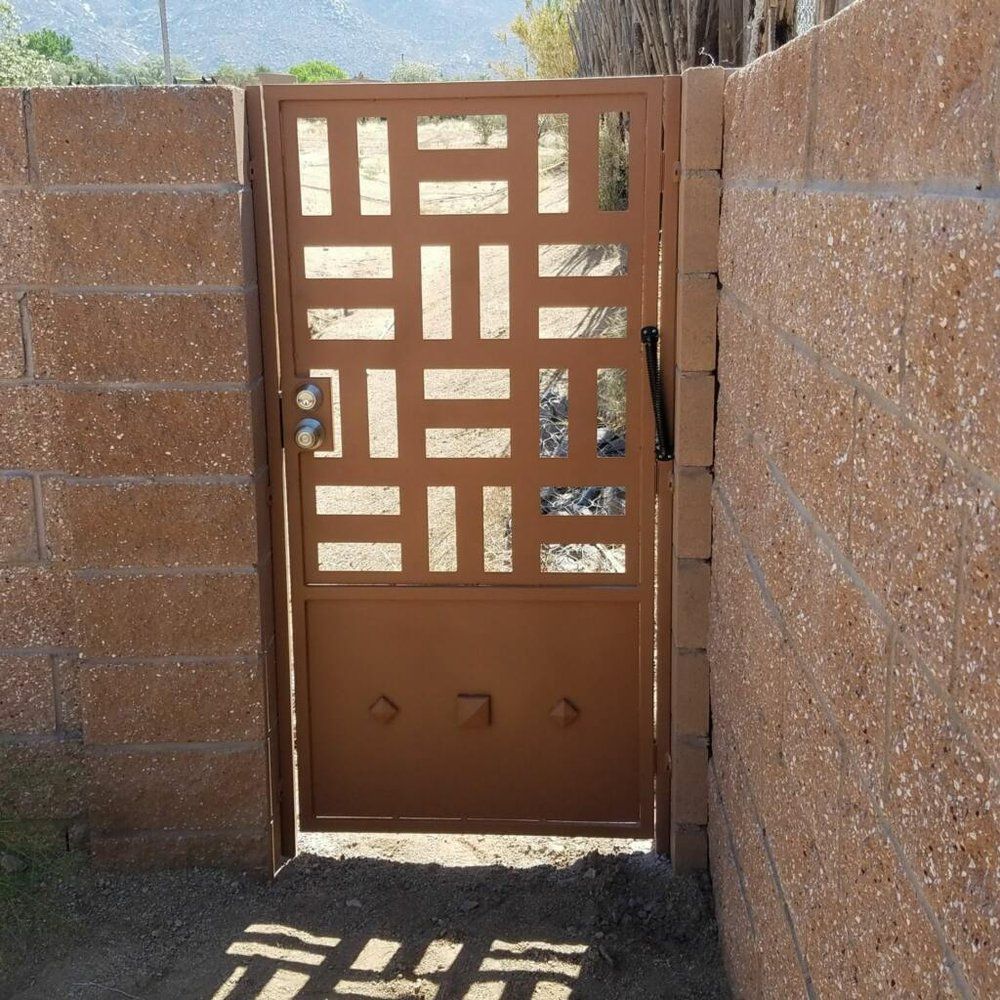 Brown metal gate with geometric cutouts in a stucco wall corridor, sunlight casting shadows