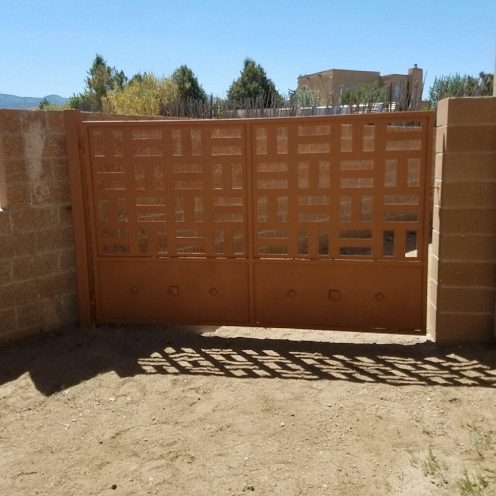 Orange metal gate with geometric cutouts between brick walls in a sunny dirt courtyard