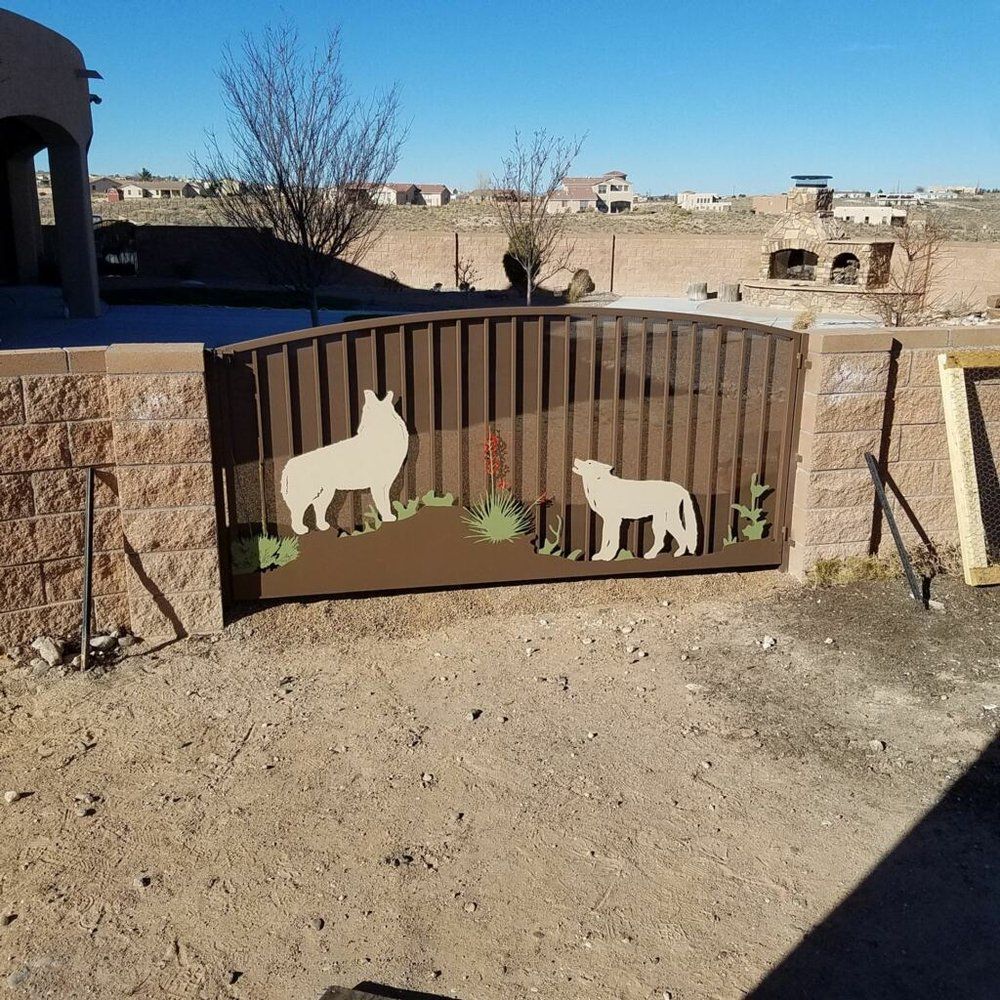 Brown gate with llama and donkey cutouts in a desert yard under a clear blue sky