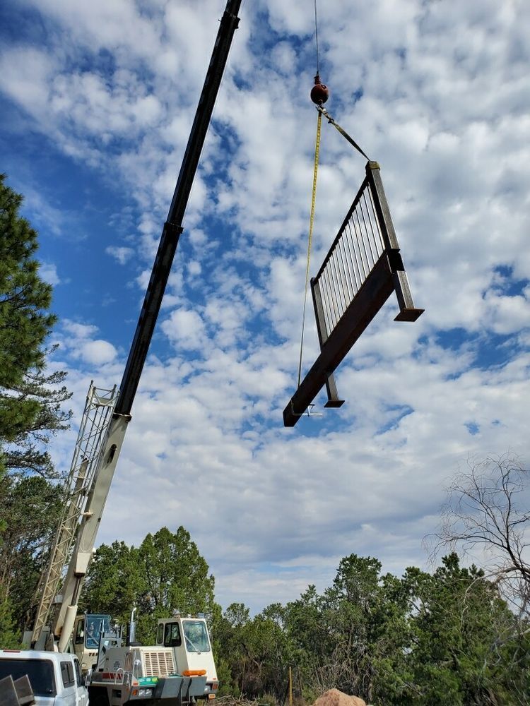 Crane lifting a large metal platform on a truck in an open outdoor work site under a cloudy sky