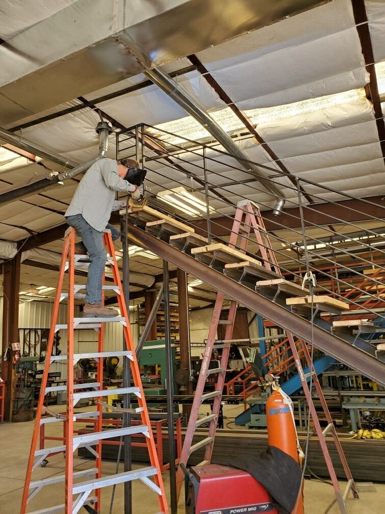 Worker standing on a ladder repairing ceiling pipes in an industrial building