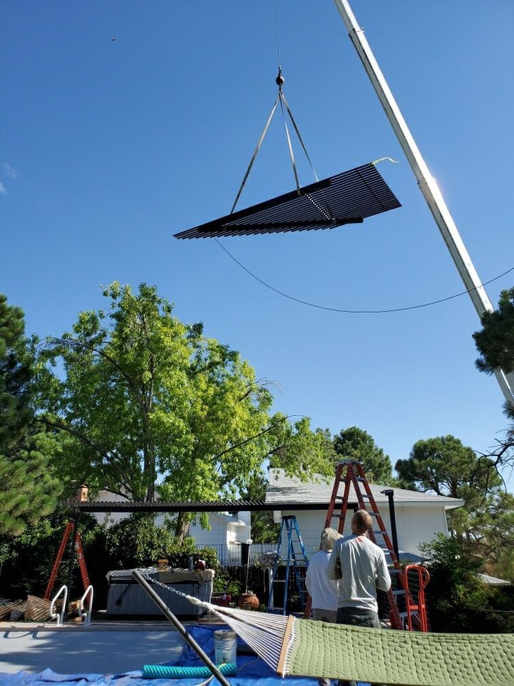 Crane lifting a large triangular panel above a backyard pool under a clear blue sky