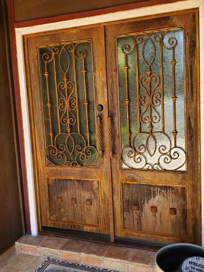 Double wooden entry doors featuring decorative iron grilles over glass panels and textured lower door panels.