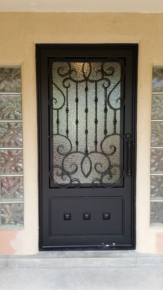 A black metal security door with an ornate iron scrollwork design over glass, flanked by columns of glass block windows.