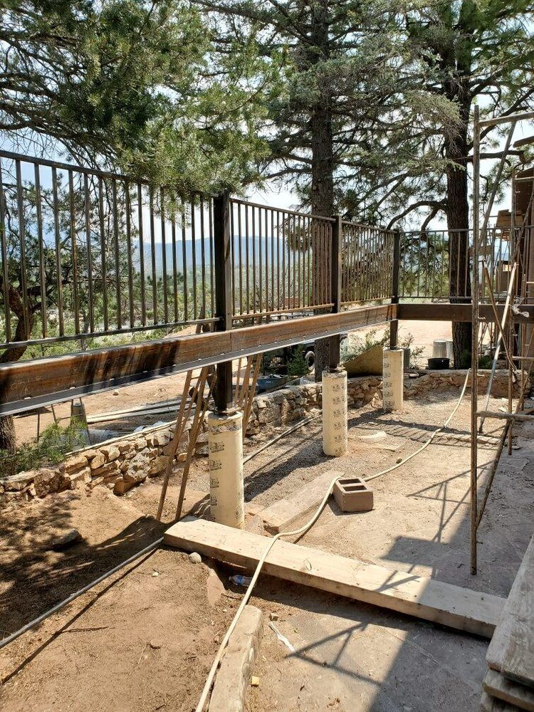 Construction site showing a metal railing supported by temporary steel beams and concrete pillars outdoors.