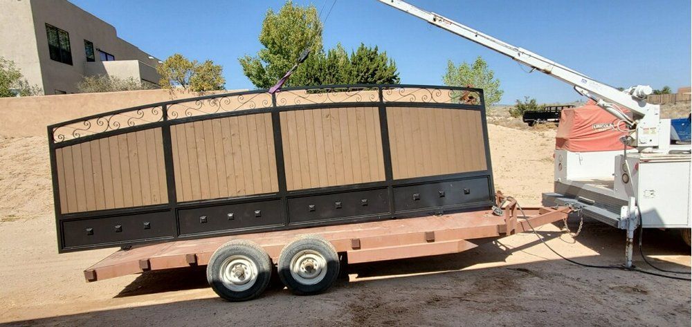A custom metal gate with wood panels sits on a flatbed trailer attached to a work truck in a desert landscape.