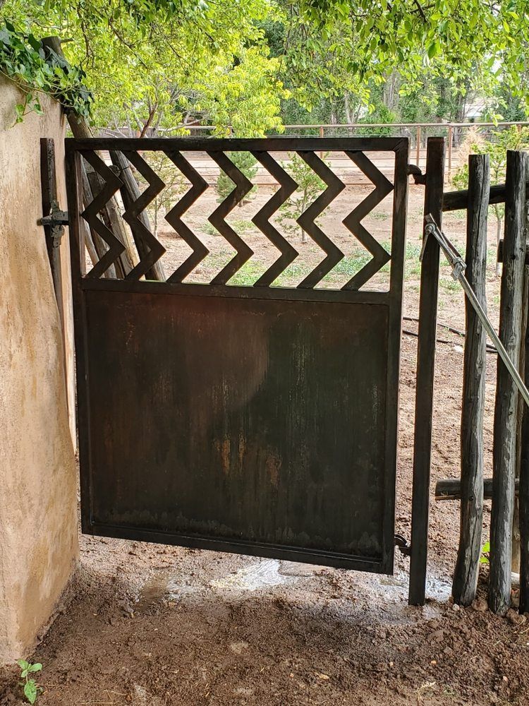 A rectangular metal gate features a solid lower panel and a top section with a black, repeating chevron pattern.