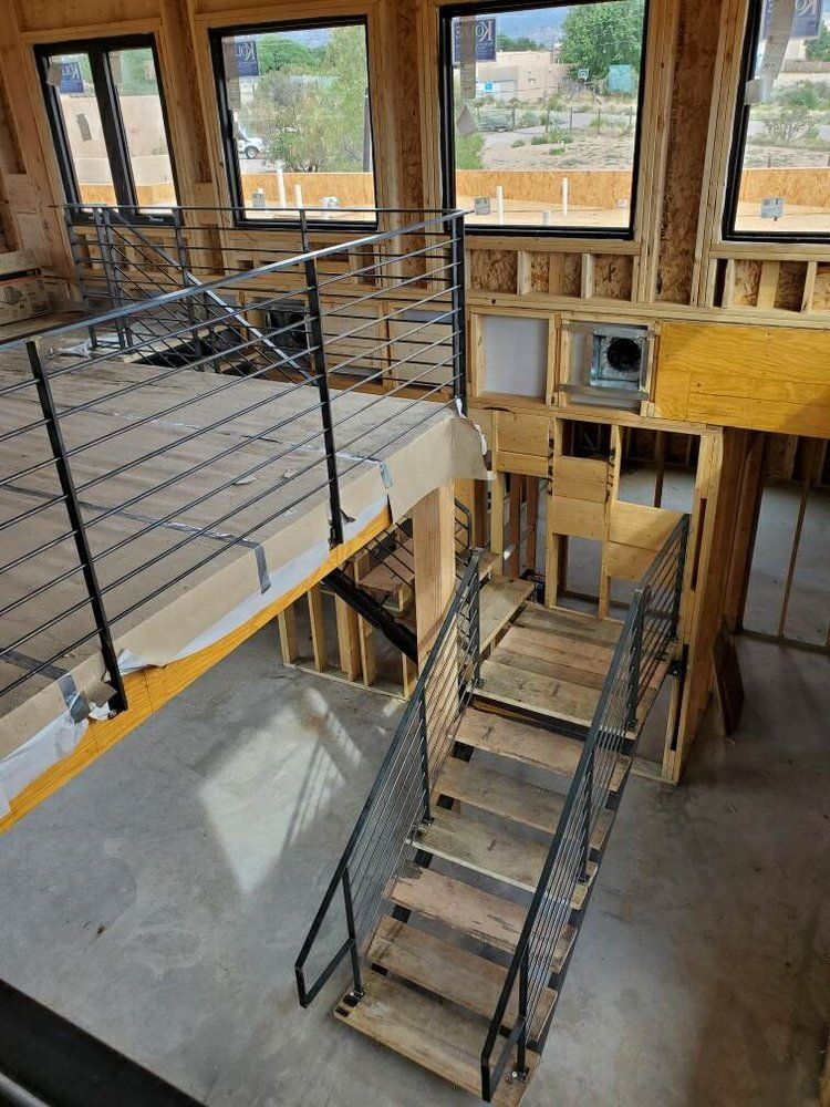 Interior view of a building under construction, featuring wooden stairs leading up to an open loft with a metal railing.
