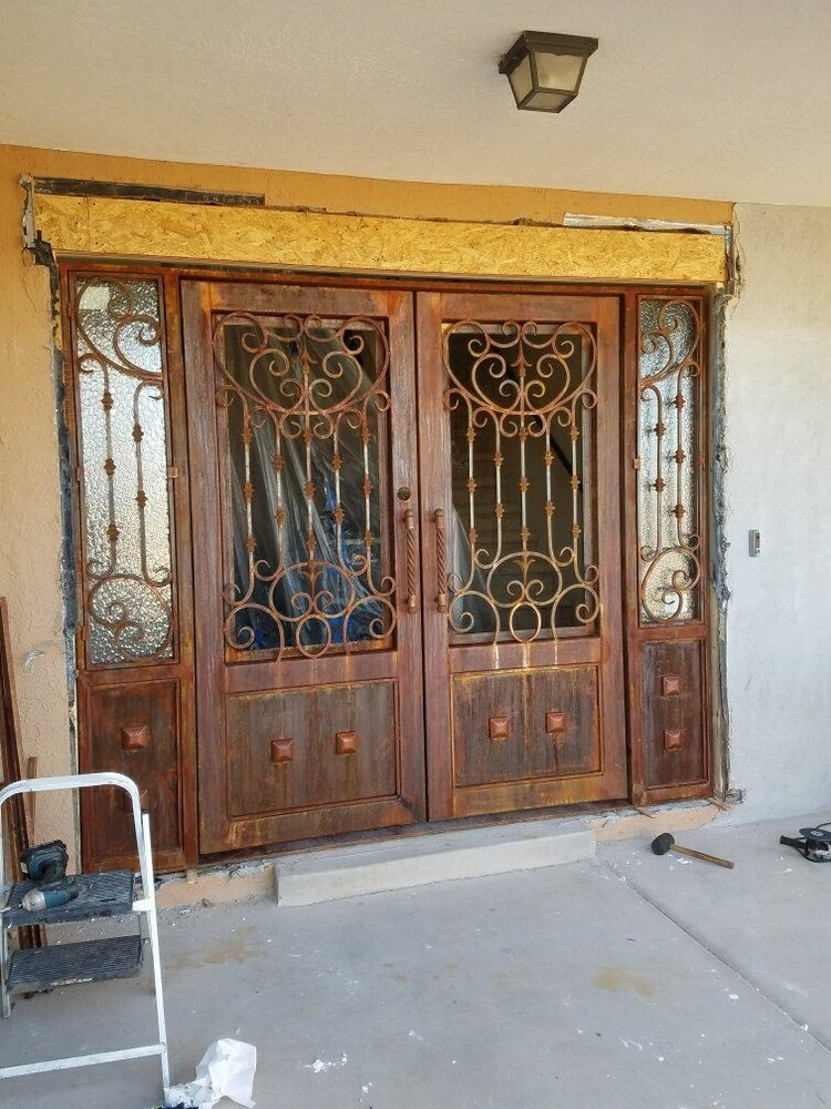 A set of double wooden front doors with ornate iron decorative grilles, currently under installation.