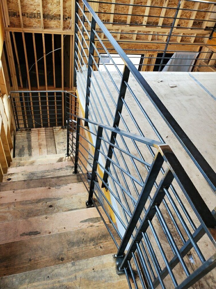 A high-angle view of an unfinished staircase with black metal railings leading up to a landing in a wooden frame building.