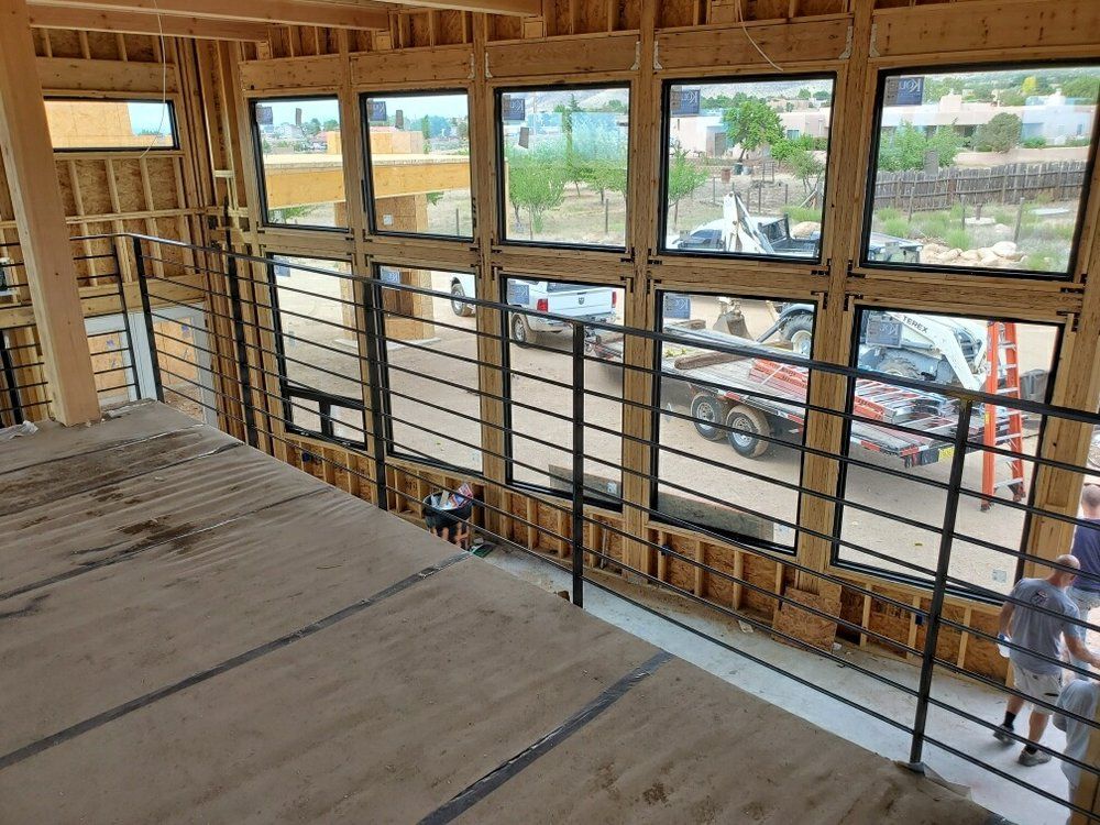An elevated wood floor overlooks a construction site through a large grid of windows, bordered by a metal railing.